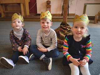 Three small children sitting on the church platform, wearing crowns they had made