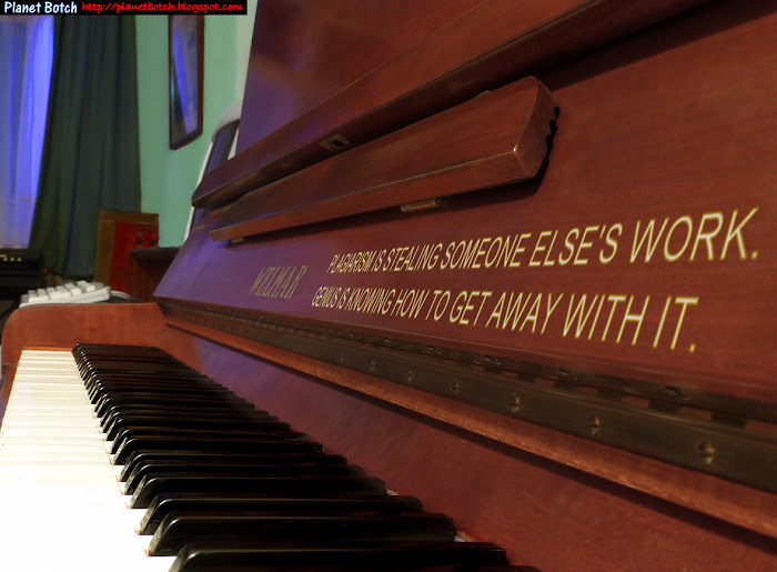 Upright acoustic piano carrying the professionally screened phrase: Plagiarism is stealing someone else's work. Genius is knowing how to get away with it.