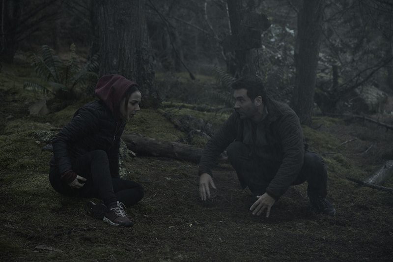 Sofia (Carolina Gaitán) and Josh (Allan Hawco) crouch on the forest floor in Andres Beltran's Quicksand