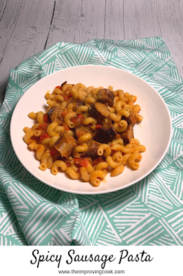 A white pasta bowl filled with spicy sausage pasta on a pale green and white patterned cloth 