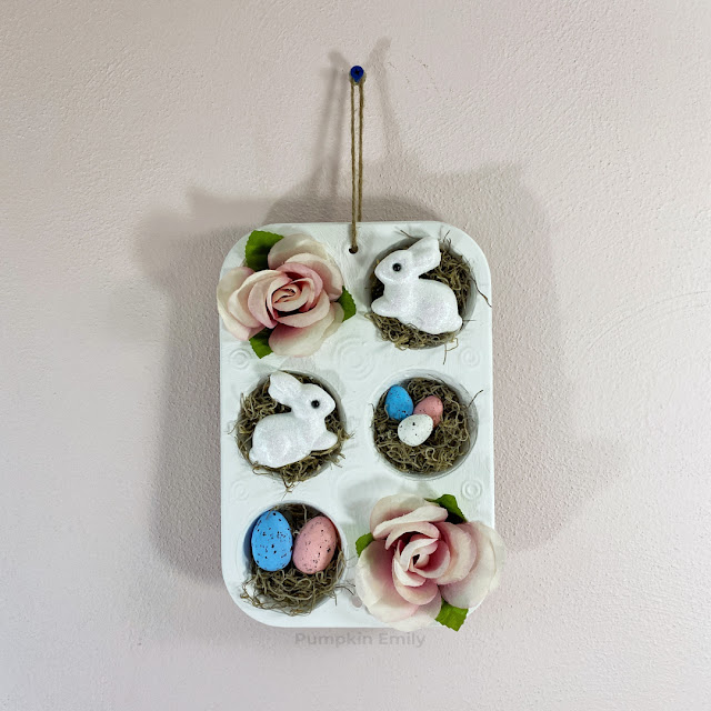 A spring white muffin pan wall decoration with bunnies, moss, eggs, and pink flowers.