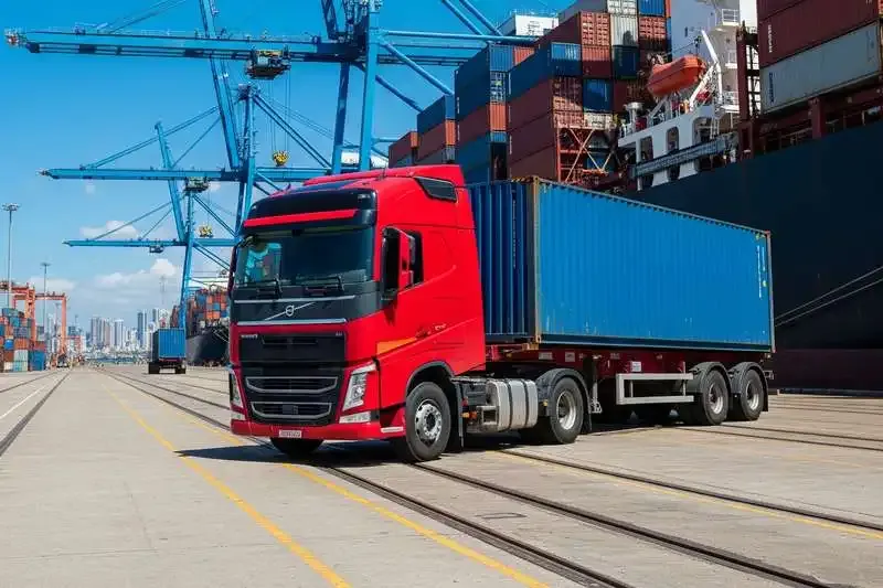 Volvo FH carregado com container no pier de um porto ao lado de um navio cargueiro