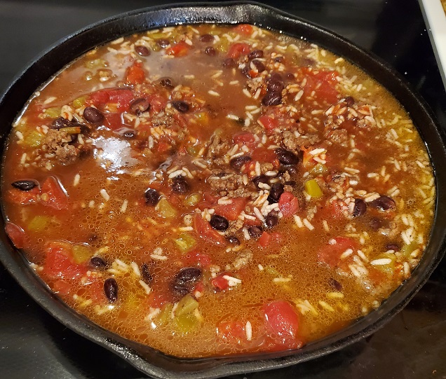 a skillet with rice, beef and beans in sauce simmering