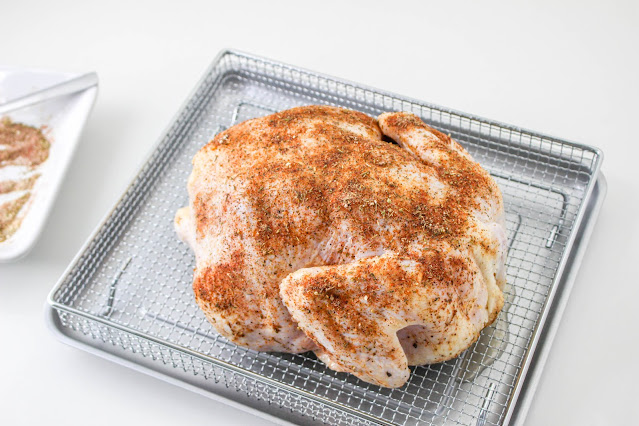 uncooked whole chicken seasoned on an air fryer basket.
