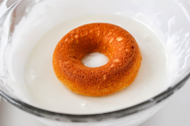 donut being dipped in a bowl of white glaze.