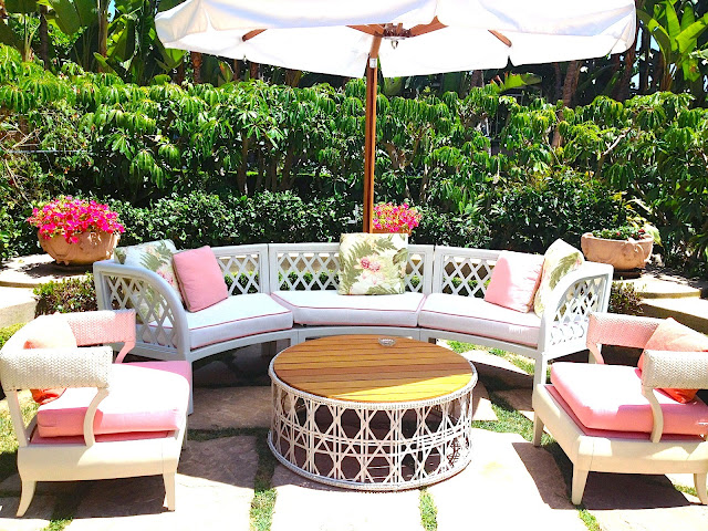 Outdoor sitting area white outdoor lounge chair with white cushions with pink piping round woven coffee table umbrella