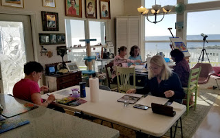 A group of women painting small watercolor paintings at tables.