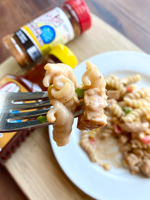 Close up bit of bbq chicken pasta salad on a fork. Background of plated salad and seasonings.