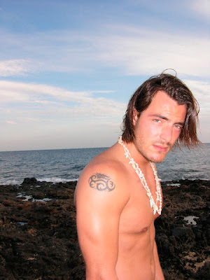 Masculine male on the beach showing his small oval shoulder tribal tattoo.