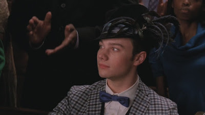 Kurt wearing a black fedora looking hat but adorned with feathers and bows