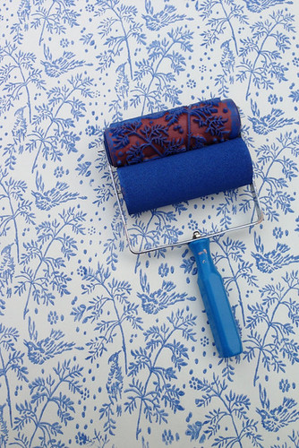 paint roller with floral plant design with blue paint on a cream coloured wall