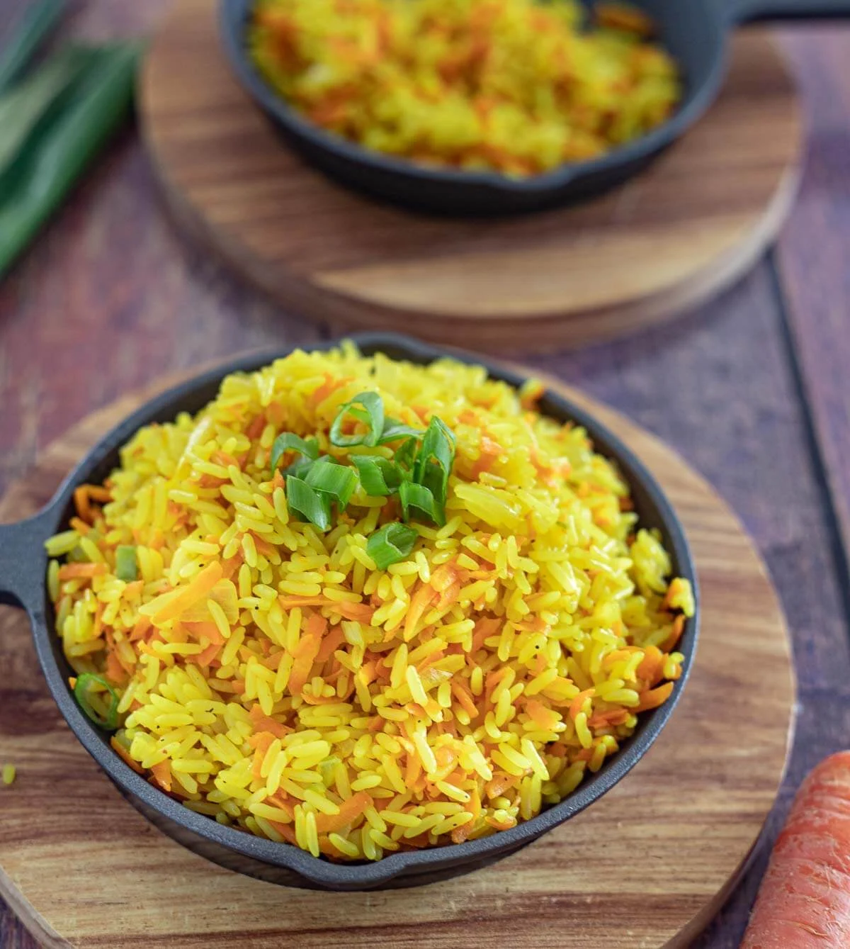 Finshed carrot rice, garnished with chopped scallion in a black cast iron dish on a brown tray.