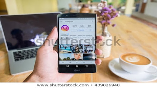 Computer, smart mobile device, white flower vase, white coffee cup on brown table.