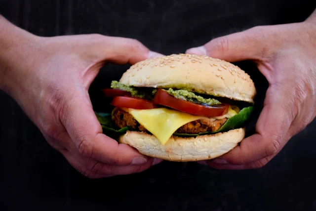 Smoky Red Pepper & Cheese Bean Burgers stacked in a burger bun with salad pesto and slice of melted vegan cheddar