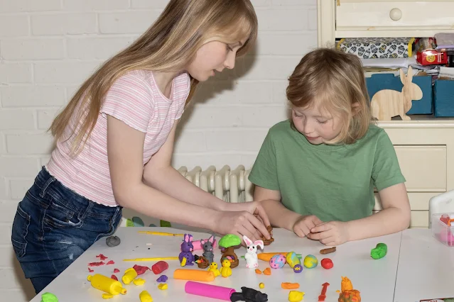 Big sister showing little sister how to make a basket out of Plasticine