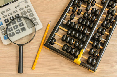 On a desk lie a calculator and an abacus with a pencil and magnifying glassw