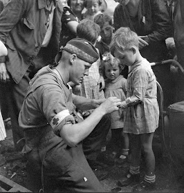 Private G-R_MacDonald-Toronto Scottish Regiment MG- giving first aid to  injured French boy-Brionne France- Aug 25 1944