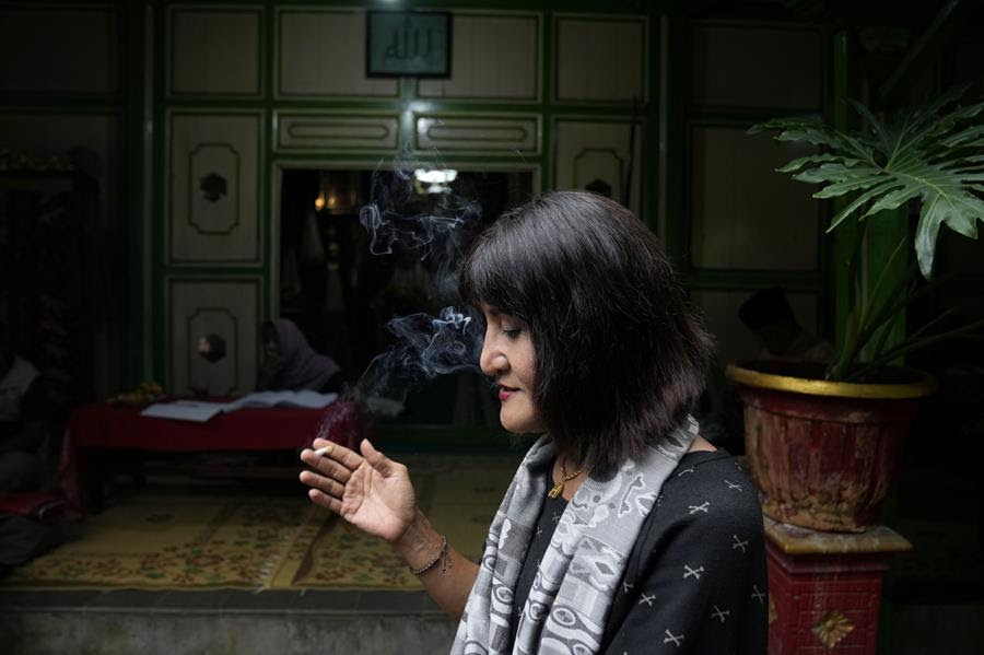 Y.S. Al Buchory, a trans woman, smokes a cigarette during an interview, with Arabic calligraphy that reads "Allah" above an entrance at Al Fatah Islamic school in Yogyakarta, Indonesia.