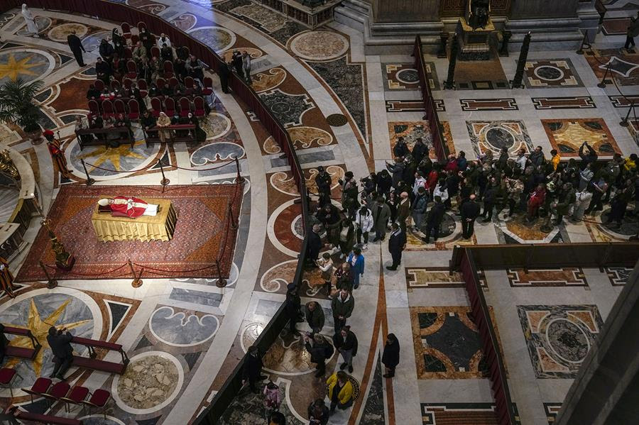 An overhead view of the inside of St. Peter's Basilica in the Vatican. There is a line of people waiting to view the late Emeritus Pope Benedict XVI.