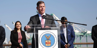 Secretary Walsh stands at a podium bearing the Department of Labor seal, at a California port.  