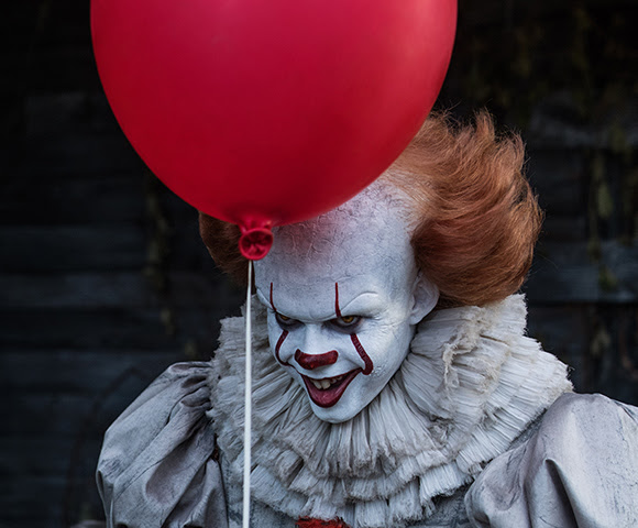 Bill Skarsgård as Pennywise the Dancing Clown holding a red balloon in front of him.