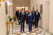 Secretary Blinken and Egyptian President Abdel Fattah El-Sisi speak to each other and walk down a corridor. Other officials walk behind them. 