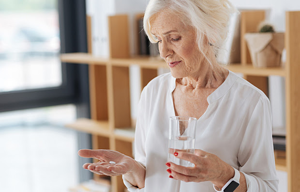 A senior woman looking down at an aspirin in her hand.