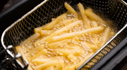 French fries fry in a basket submerged in bubbling oil.