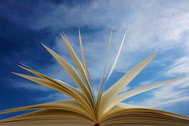 Photo of an open book, the pages fanning open, against a blue sky.