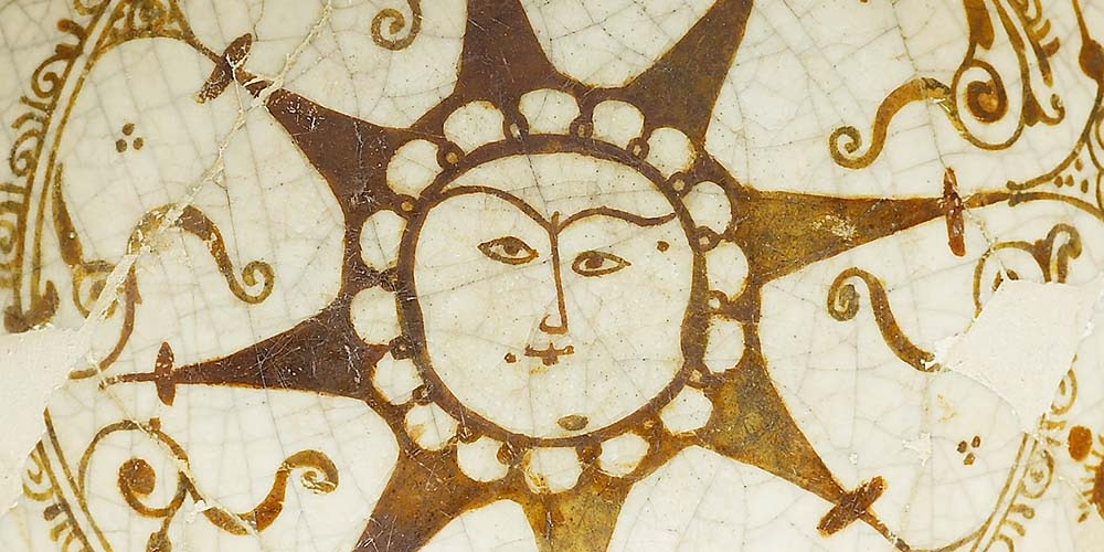 A detail from a decorated bowl which depicts a human-faced sun.