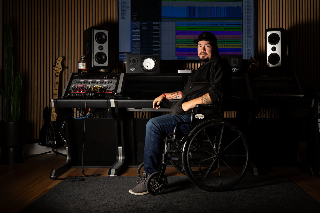 Robert Perez sits in a wheelchair in front of music production equipment and a guitar.