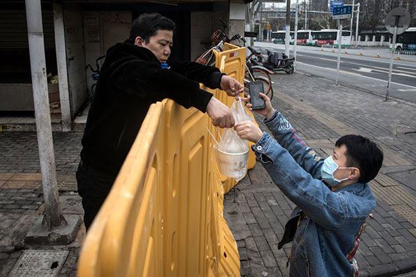 A man wearing a mask sells breakfast to nurses behind a makeshift barricade wall built to control entry and exit to a residential compound in Wuhan