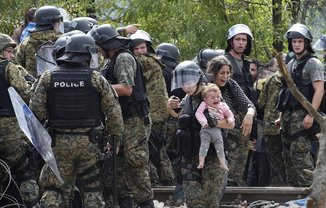 A member of the Macedonian special police forces holds a baby as migrants try to cross into Macedonia near the southern city of Gevgelija, The Former Yugoslav Republic of Macedonia, 22 August 2015 Photo: EPA/Georgi Licovski