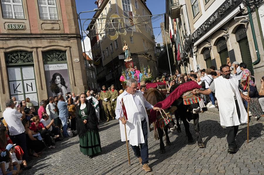 People guide ox-pulled floats with sacred images of Mary through the town of Lamego. People are gathered to watch the procession.