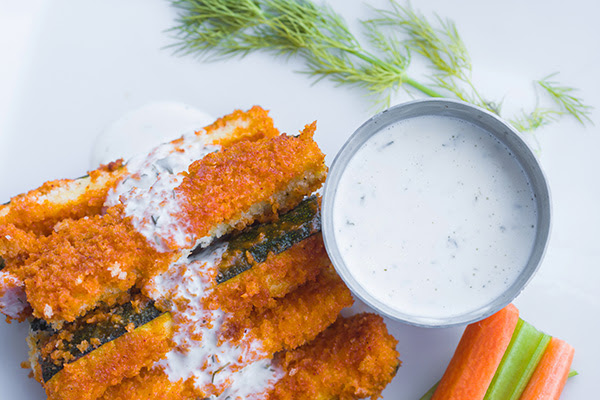 close up photo of buffalo zucchini sticks with a bowl of tzatziki dip