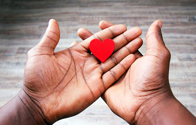 Hands holding a red wooden heart.