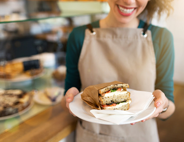 Close up of a barista holding up a plate with a sandwich