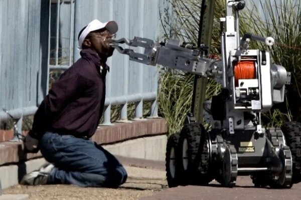 Photo of weird SFPD Robot putting something in a handcuffed man's mouth.