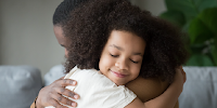 A young girl being embraced by her mother.