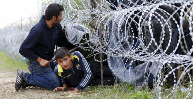 Refugiados sirios cruzan debajo de una alambrada con cuchillas e la frontera entre Hungría y Serbia, cerca Röszke.- REUTERS / Laszlo Balogh