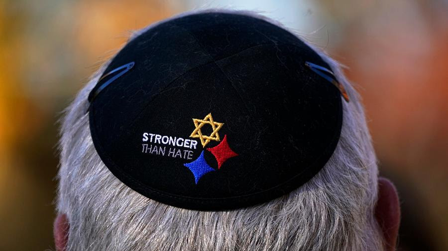 Kris Kepler attends a commemoration ceremony in memory of the 11 worshippers killed four years ago at the Tree of Life synagogue. He is wearing a black kippah that says "Stronger than hate" with three starts beside the text. The topmost start is a star of David.