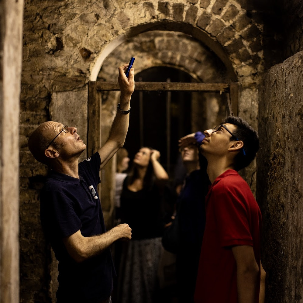 Tour guide using torch to direct tour group's attention up to arched ceiling in station 