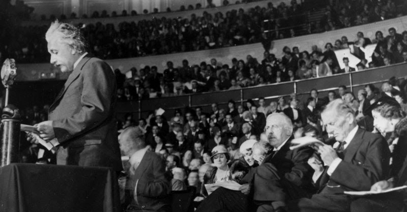 Albert Einstein speaking at a podium in an auditorium