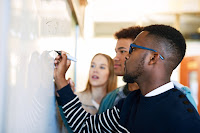 College students finish up a math problem at the whiteboard.