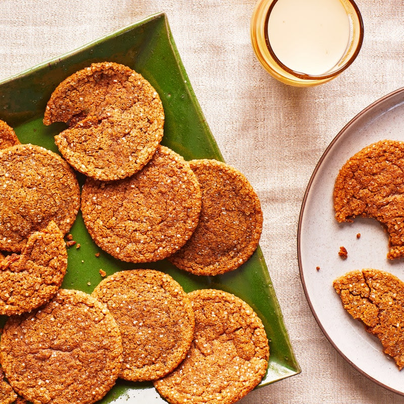 Green plate with a pile of molasses cookies, some broken in half, with one on a side plate with a bite taken out.