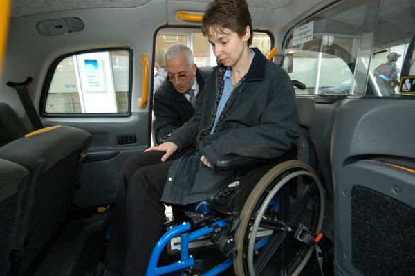 Taxi driver assisting wheelchair user to get into a modern taxi