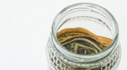 Dollar bills are visible through the mouth of a glass tip jar.