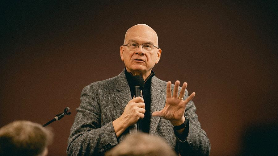 Tim Keller speaks to a group. He is holding a microphone in one hand and gesturing with the other.