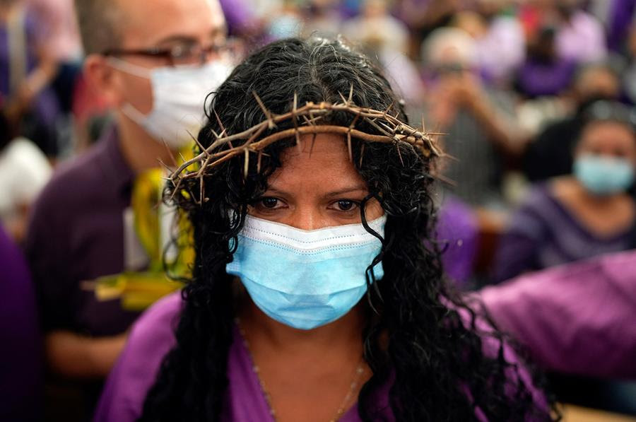 A woman wearing a crown of thorns, purple clothing and a surgical mask takes part in Holy Week celebrations.
