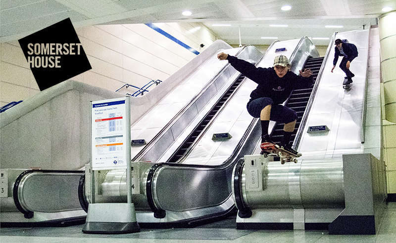 A photo by Robert Gifford. Two skateboarders skate down escalators at a London Underground station.